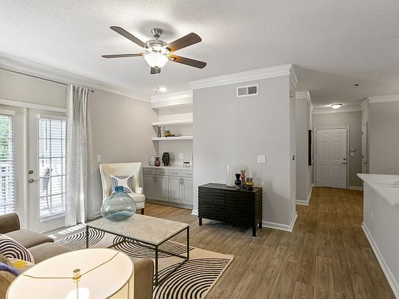 Open living room with modern furniture, wood inspired flooring, ceiling fan with light with partial view of the kitchen