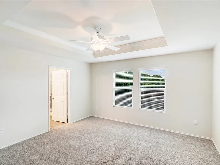 Spacious room featuring a tray ceiling with a ceiling fan, plush carpet flooring, and two windows equipped with blinds
