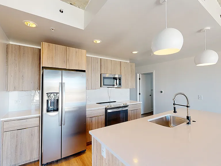 Apartment kitchen with stainless steel appliances, quartz countertops and wood-style flooring.
