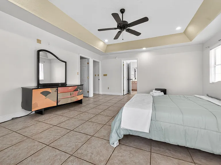 Spacious bedroom with tiled floors, ceiling fan, and ample room for furnishings, plus easy access to a nearby bath.