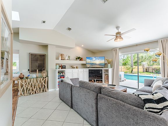 Living room with large sectional sofa, electric fireplace, 58" smart TV, pool view, and a variety of board games.