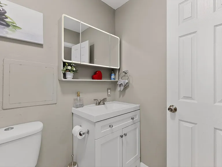 A clean primary bathroom featuring a toilet, vanity and medicine cabinet, with neutral-colored tiles and bright lighting.