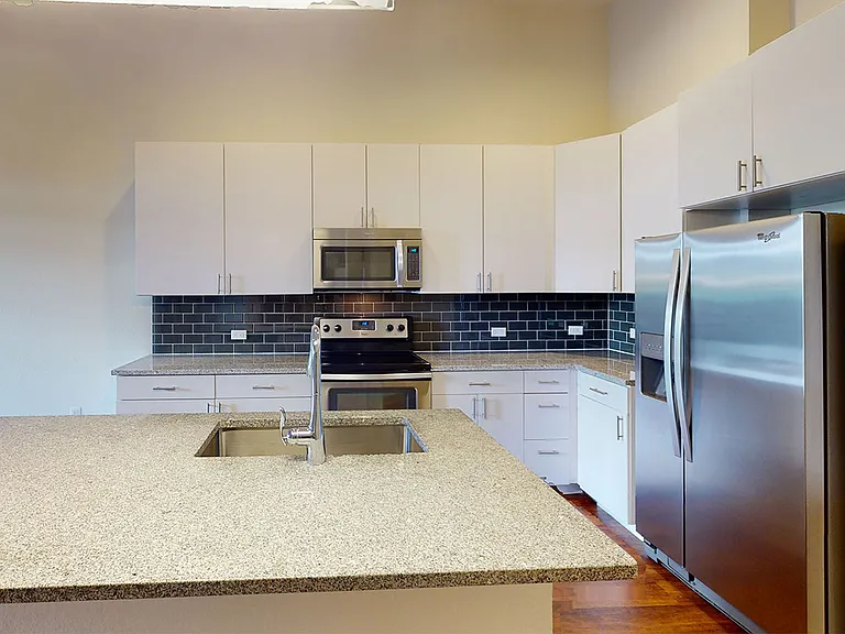 Apartment kitchen with stainless steel appliances, granite countertops and wood-style flooring.
