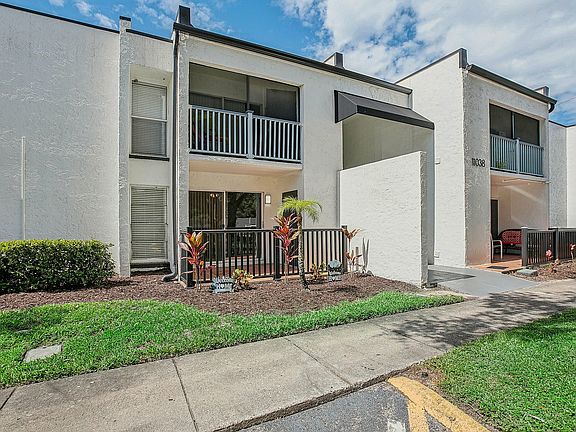 Charming modern apartment exterior with welcoming balconies, lush landscaping, and a bright sky backdrop.