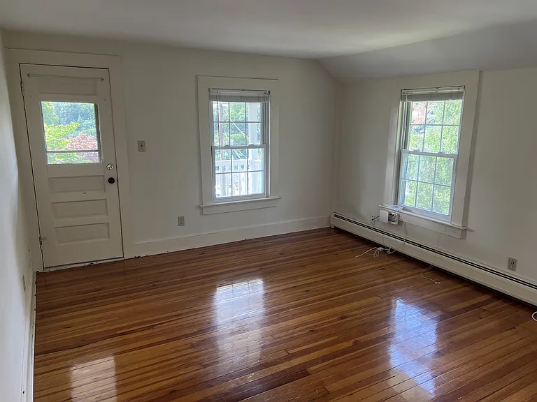 Spacious living room area. The door to the porch straight ahead. Several window for light.