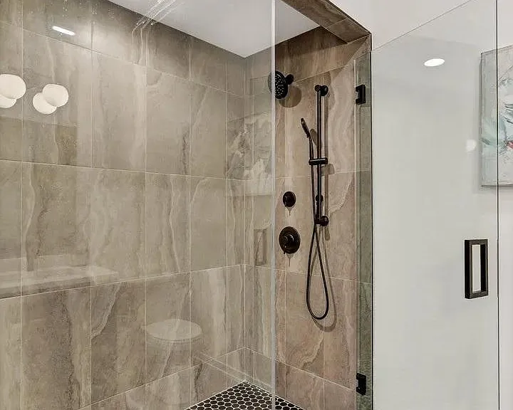 Oversized Shower: Floor-to-ceiling marble-look tile, frameless glass enclosure, matte black fixtures