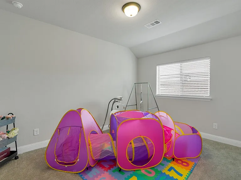 Carpeted room featuring a single window with blinds, ceiling-mounted light fixture, and a built-in smoke detector