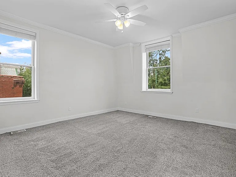 Spacious second-floor bedroom with 10-foot ceilings, two windows with 2-inch wood Venetian blinds, soft carpeting, crown molding, and a ceiling fan with lighting.