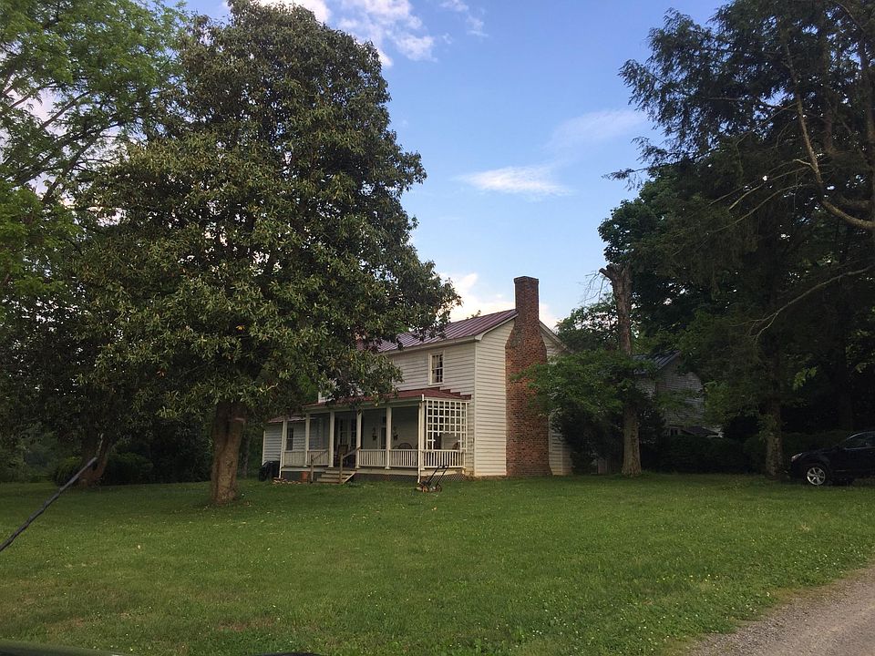 The large farmhouse is dwarfed by ancient trees.