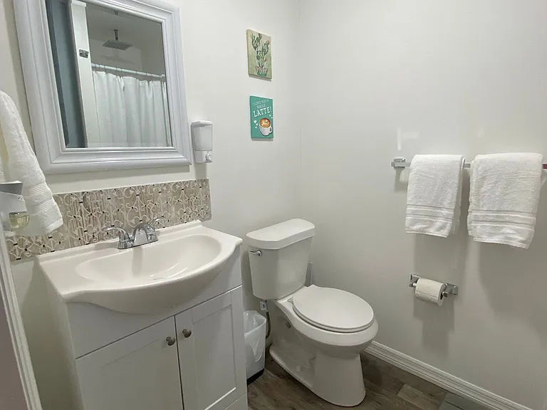 Spotless bathroom includes a mirror, sink, toilet, shower, towel racks, and essential supplies