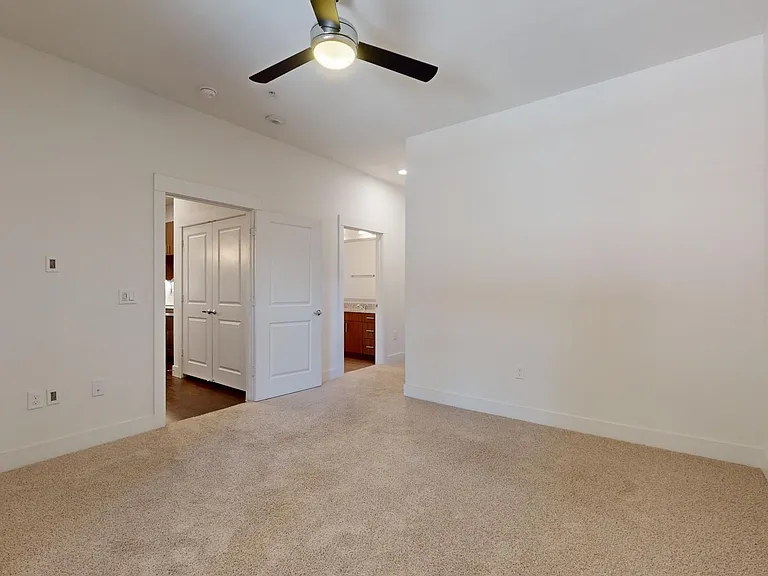 Spacious apartment bedroom with large closet, attached bathroom, and plush carpet flooring.