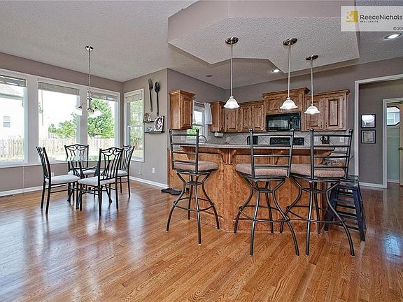 Large Kitchen w/Hardwood Floor, Island, Breakfast Bar, Upgraded Tile Backsplash, Designer Black Appliances, Corian, Built-in's, Pantry, Breakfast Room & Door to Patio!