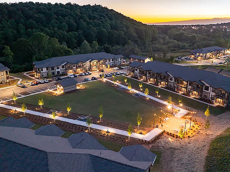 Stunning aerial view of a beautiful apartment complex nestled in nature, featuring modern buildings, well-lit pathways, and serene green spaces perfect for relaxation.