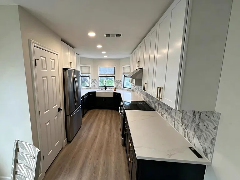 Galley kitchen with ample shaker cabinetry, quartz-style counters, stainless appliances, and a farmhouse sink by windows.