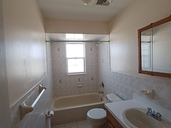 Spacious full bathroom with a bathtub and shower combo, tiled flooring, and a window that brings in natural light. Includes a sink vanity, mirror, and clean finishes throughout for a practical and functional setup.