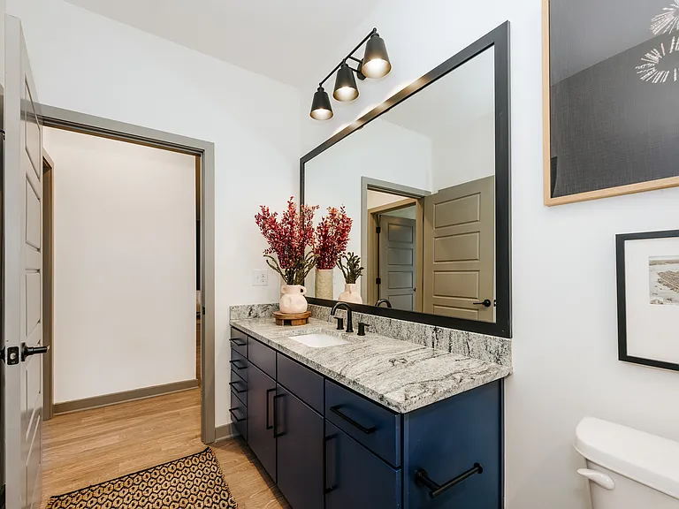 Modern apartment bathroom with granite countertops, matte black fixtures, and spacious vanity storage.