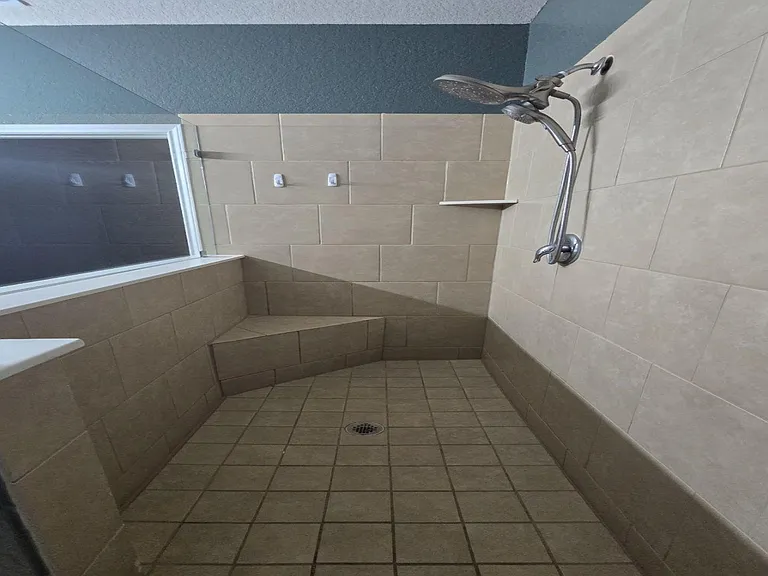 Walk-in tiled shower with built-in bench, rain-style showerhead, and glass partition for an open, accessible layout.