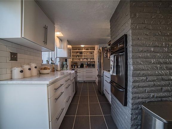 Galley kitchen with Carrera Marble countertops, Built-in oven and gas stovetop. Coffee bar and open shelving.