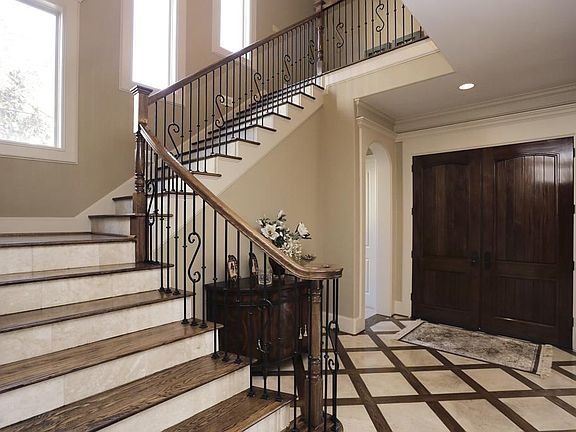 Dramatic double door entry with custom inlaid flooring, wrought iron staircase and hardwood treads.