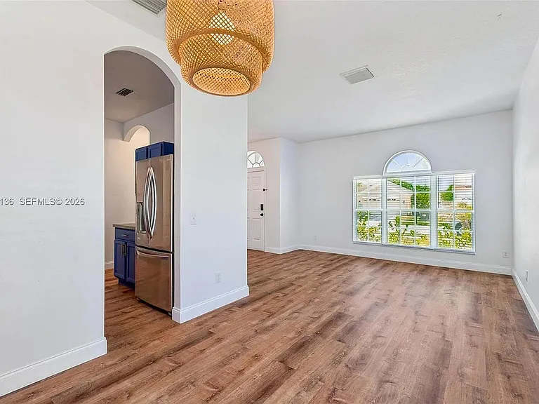 Open living area with wood-look flooring, large window for natural light, and direct access to the kitchen and entry.