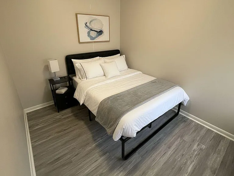 Furnished bedroom with a full bed, nightstand and lamp, plus durable plank flooring and neutral walls for easy setup.