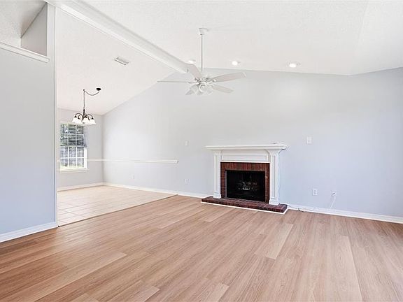 Unfurnished living room with high vaulted ceiling, light hardwood / wood-style floors, a fireplace, and ceiling fan with notable chandelier