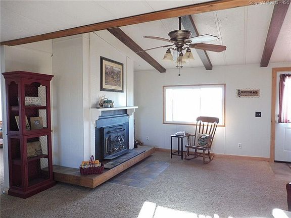 Beautiful fireplace and dark beams on the ceiling, which has a ceiling fan.