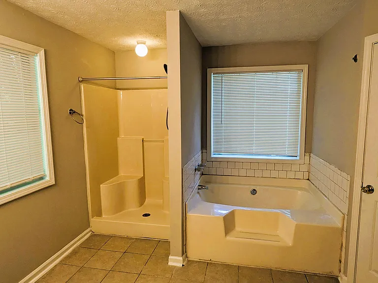 Full bathroom with separate shower and soaking tub, tile flooring, and two windows with blinds for added ventilation.