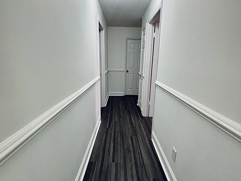 Long interior hallway with durable dark flooring, wainscoting trim, and multiple doorways for easy access to rooms.