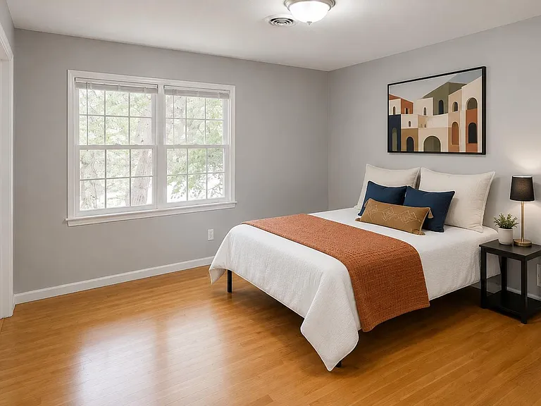 Spacious bedroom with hardwood floors, a large window for natural light, and room for a full bed plus nightstand.