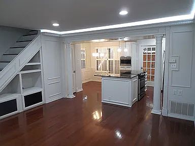 Open-concept living, dining, and kitchen area with hardwood floors, recessed lighting, architectural columns, and built-in storage