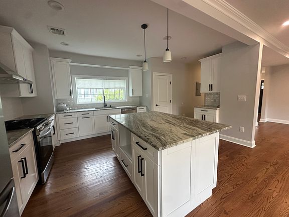 Designer kitchen with large granite island, new stainless-steel appliances, and modern black hardware.
