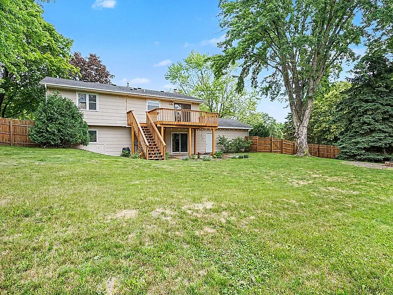 Fully fenced backyard with firepit, raised garden bed, perennial flowers, string lights, and large deck.