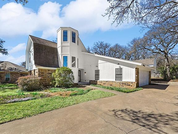 View of front of house with stone siding, concrete driveway, a gambrel roof, and a garage