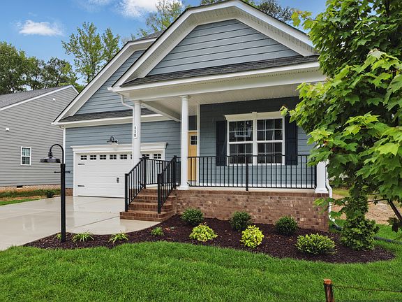 A blue Somerset Hill suburban house with a front porch, garage, green lawn, small shrubs, and a tree