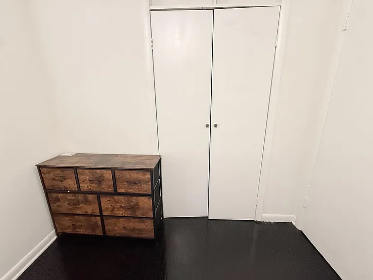 Clean bedroom area with dark flooring, a storage dresser, and a large double-door closet for convenient organization.