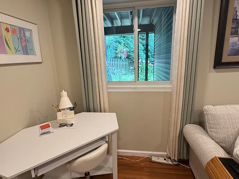 View looking out window with desk. Living room on right & bedroom on left.