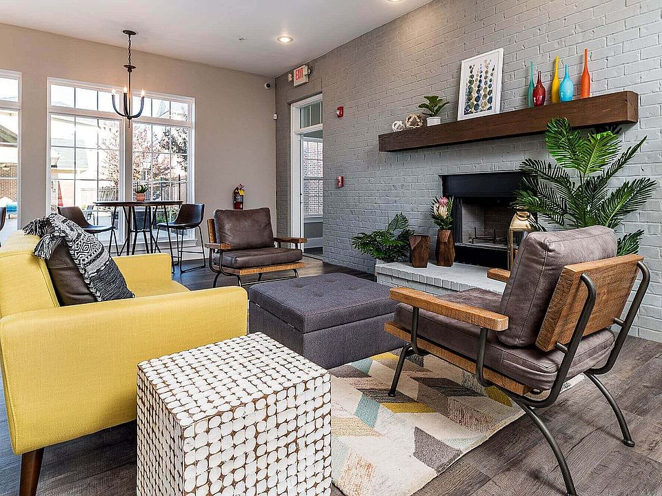Inviting living room with modern decor, featuring a cozy fireplace, vibrant yellow sofa, stylish leather chairs, and natural light from large windows.
