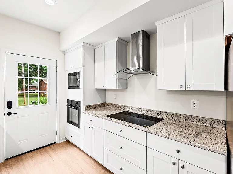 Streamlined kitchen with ample white cabinetry, granite counters, and built-in oven/microwave plus a smooth cooktop.
