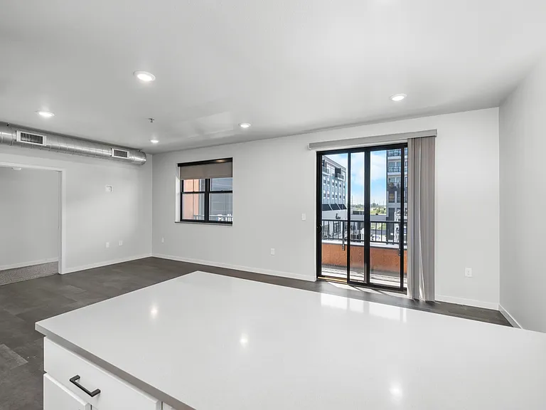 Modern open-concept living space with sleek finishes, large windows, and balcony access offering urban city views. Modern open-concept living space with sleek finishes, large windows, and balcony access offering urban city views.