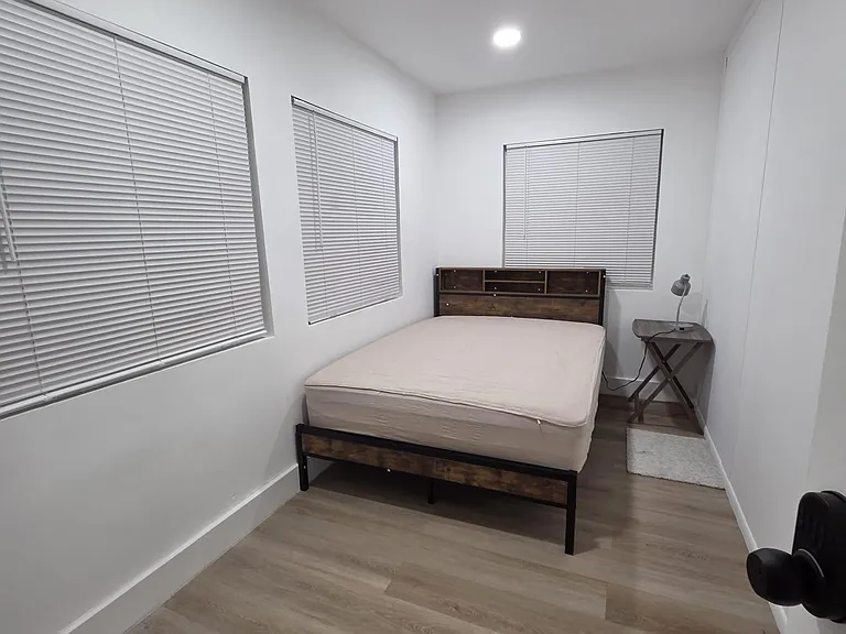 Furnished bedroom with a platform bed, side table, and multiple windows with blinds over easy-care flooring.
