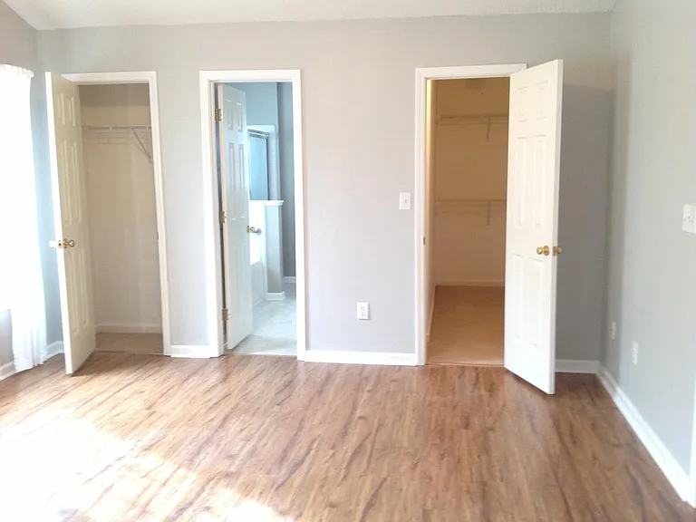 One regular clothes closet plus a deep walk-in with hanging clothes and shelves along two sides and small nook of recessed shelves.