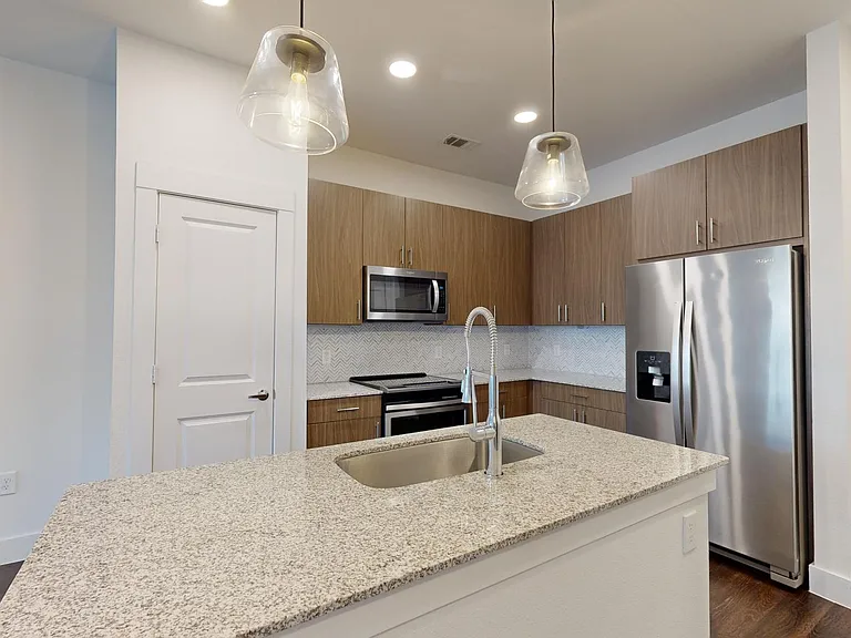 Apartment kitchen with stainless steel appliances, granite countertops, and wood-style flooring.