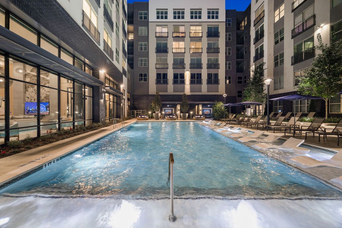 Luxury apartment complex with a stunning outdoor swimming pool, surrounded by elegant lounge chairs and ambient evening lighting.