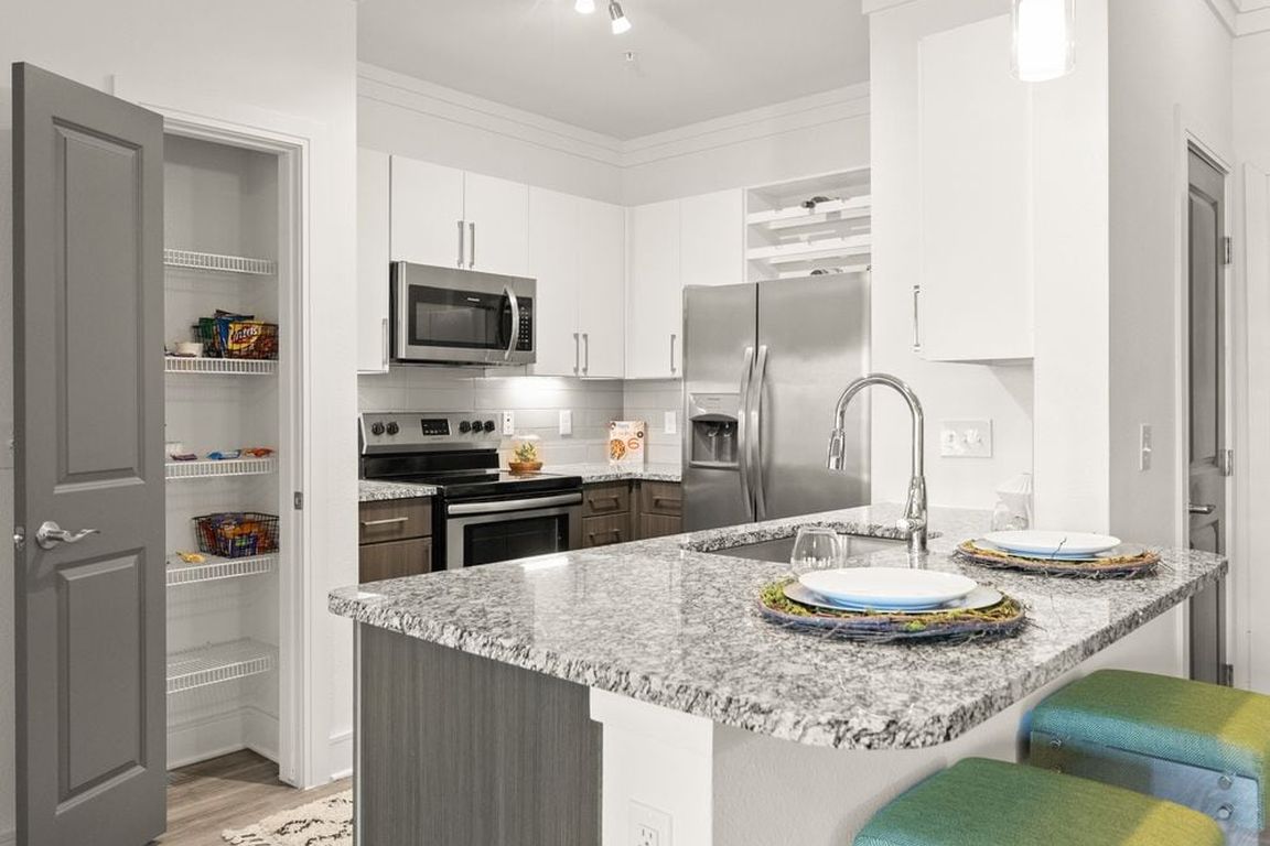 Kitchen with white and espresso cabinetry, speckled granite countertops, stainless steel appliances, and hard surface flooring