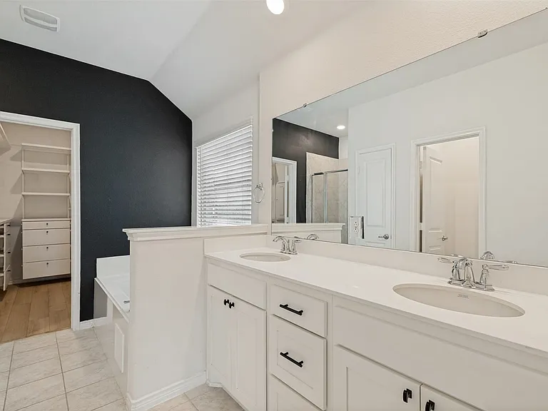 Double vanity with white cabinetry and integrated sinks, a large wall-mounted mirror, tiled flooring, and a window with blinds