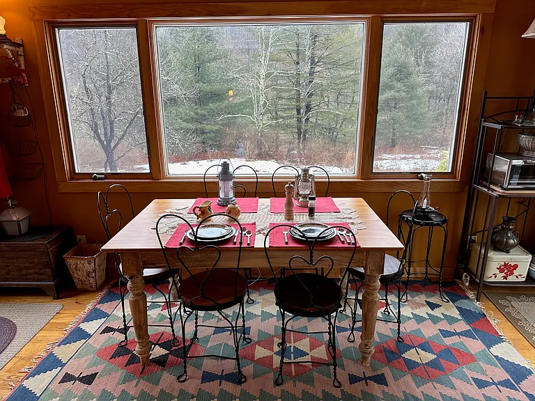 Dining Area with farm table with 6 vintage ice cream parlor chairs and large picture window with casement windows on both sides overlooking Woodland Valley.