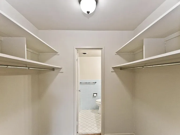 Master walk-in closet with shelving on both sides. Door to the en suite bathroom with shower in the distance.