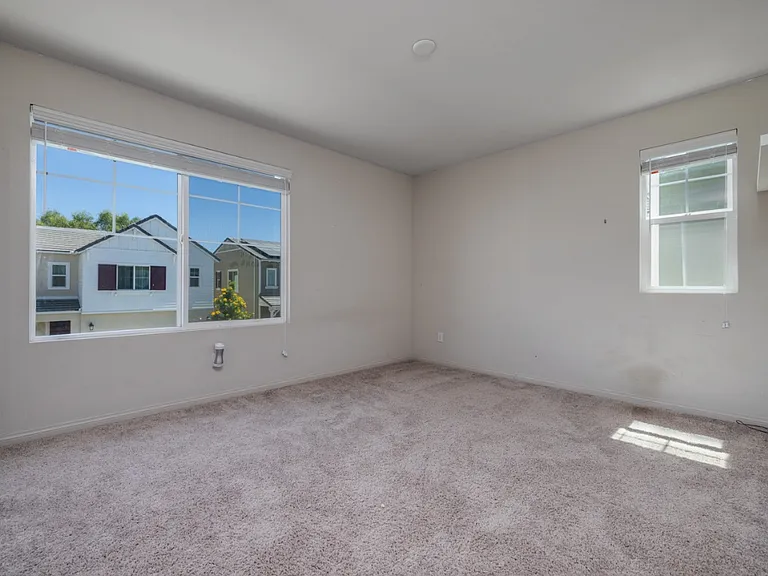 Another view of the first upstairs bedroom featuring windows facing east and south, filling the room with beautiful natural light throughout the day. Soft carpet flooring and neutral walls create a bright, cozy, and inviting atmosphere.