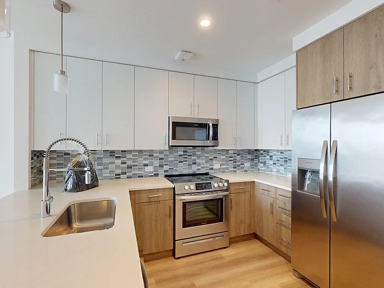Apartment Kitchen with Stainless Steel Appliances, White Stone Countertops and Wood-Style Floors